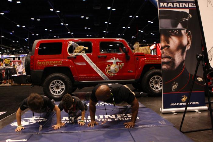Two young fans do push-ups with at Marine at the United States Marine Corps booth at the UFC Fan Expo